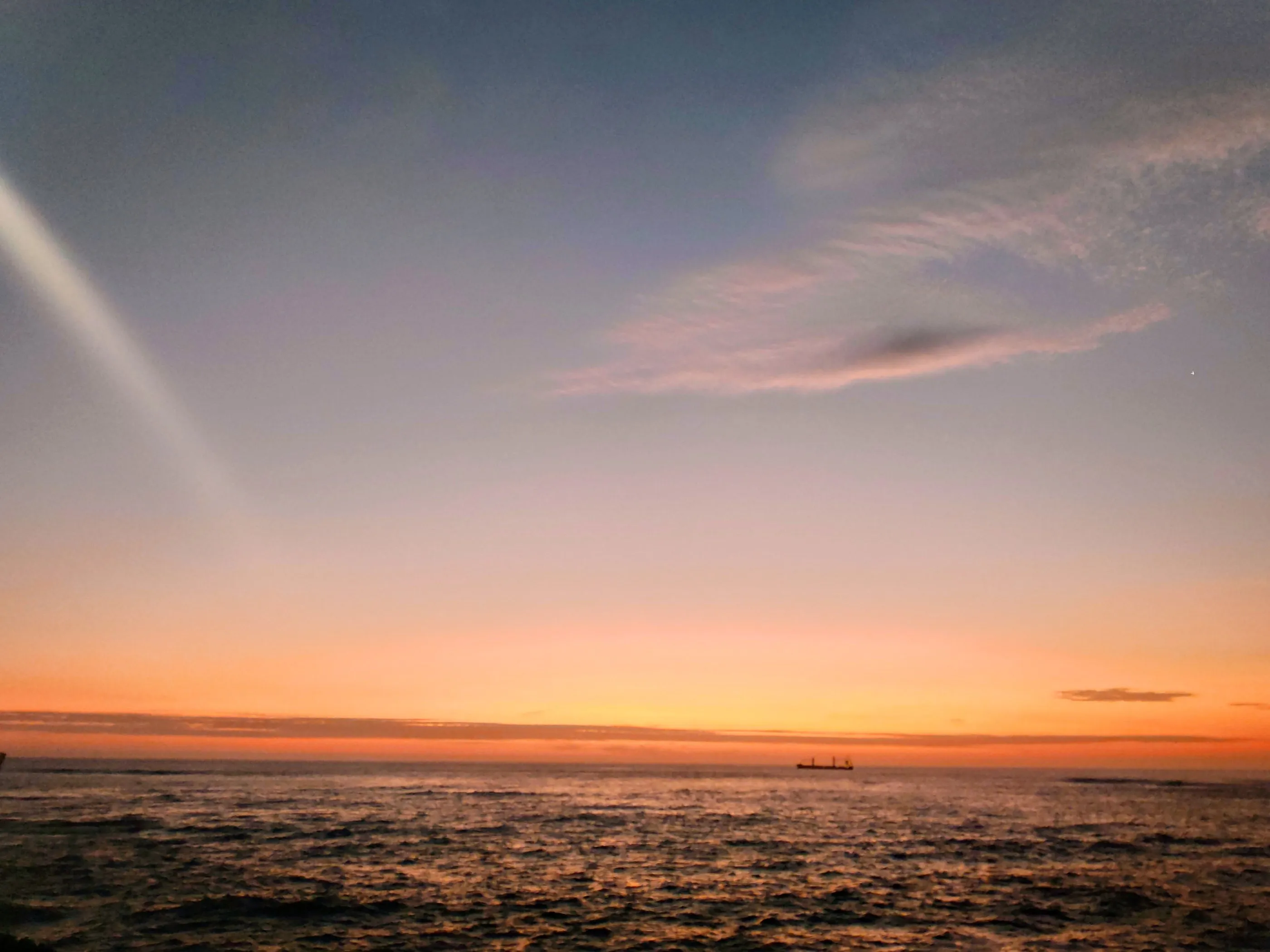 The sun setting over a calm Pacific Ocean, the sky fading from orange to deep blue